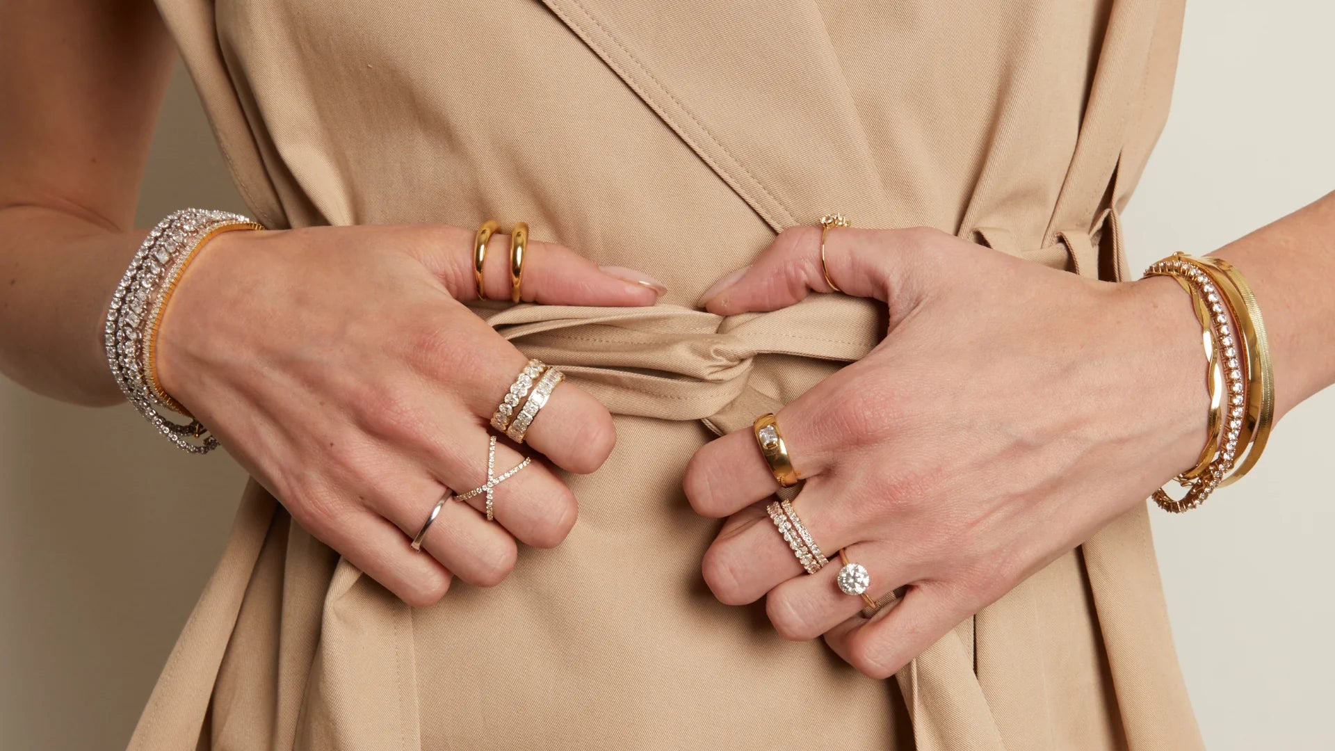 Woman wearing layered gold and diamond rings, tennis bracelets and bangles styled with a beige wrap dress — fine jewelry collection