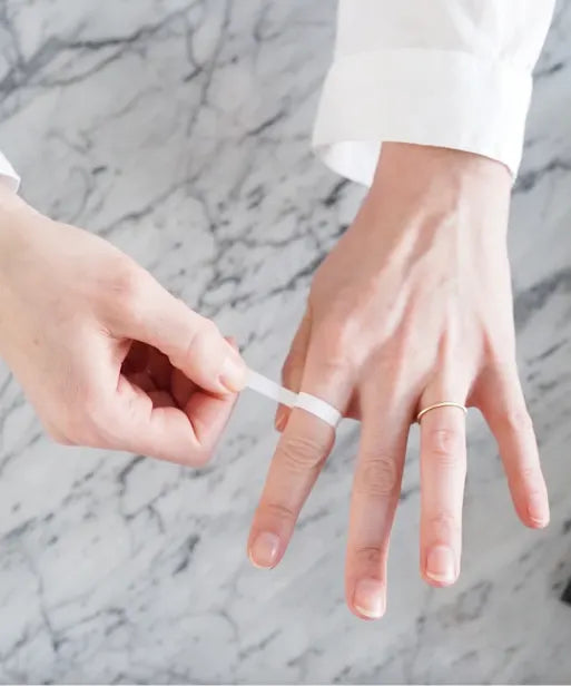 Paper strip wrapped around the base of a finger, showing a ring sizing step for the LeMing size guide.