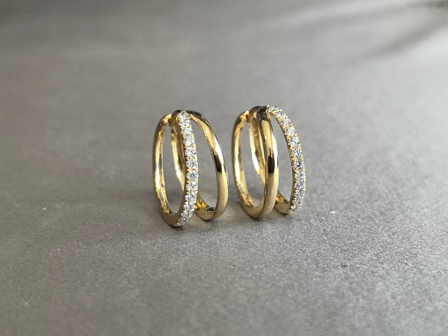 Pair of gold double hoop earrings with one pavé diamond hoop and one polished gold hoop, photographed on a gray fabric background.