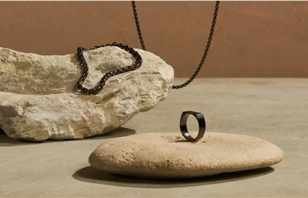 Black titanium ring and black chain necklace displayed on natural stone, minimalistic jewelry styling