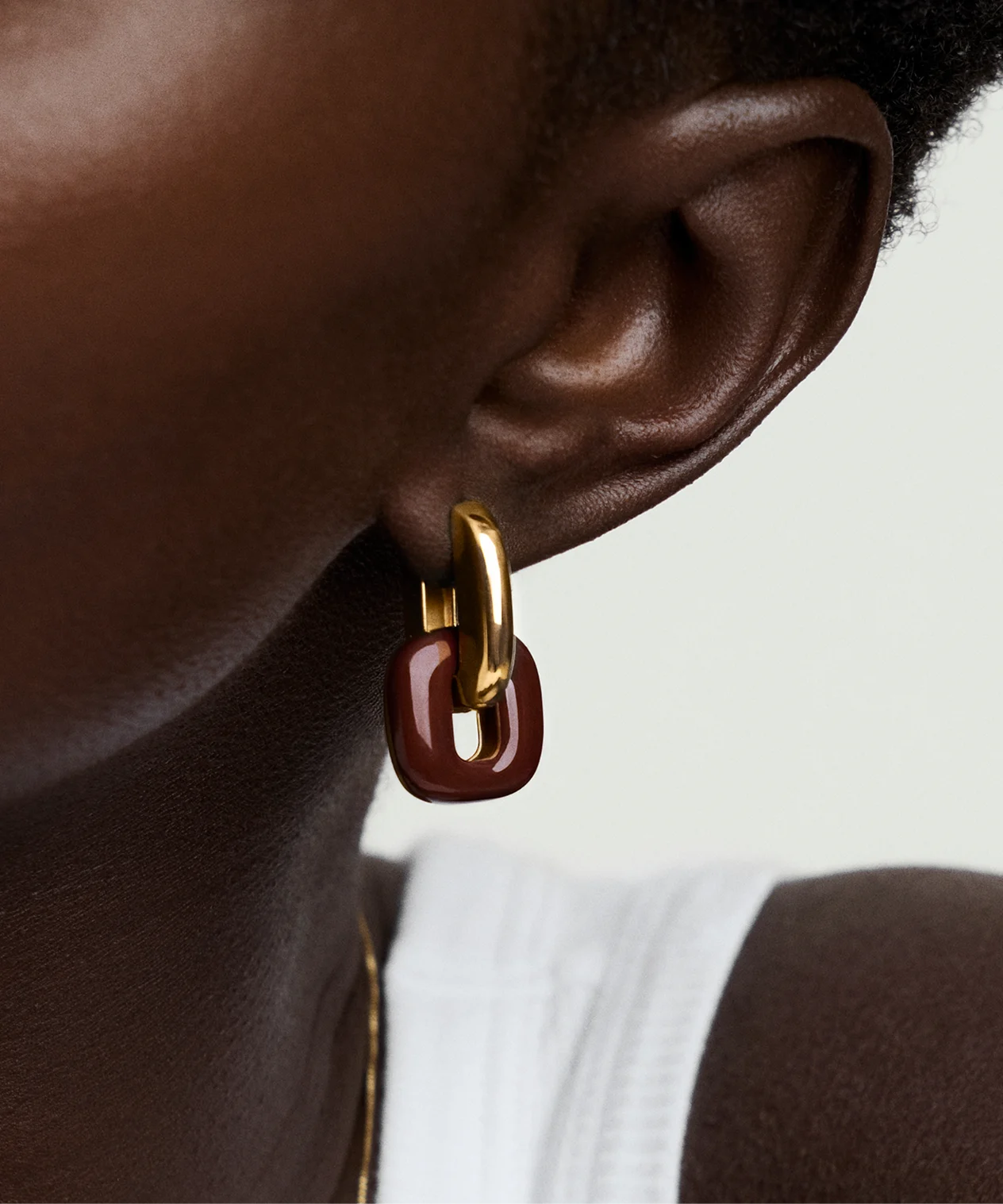 Close-up of LeMing gold and red drop earrings worn by model with dark skin, showcasing modern minimalist design and luxurious finish