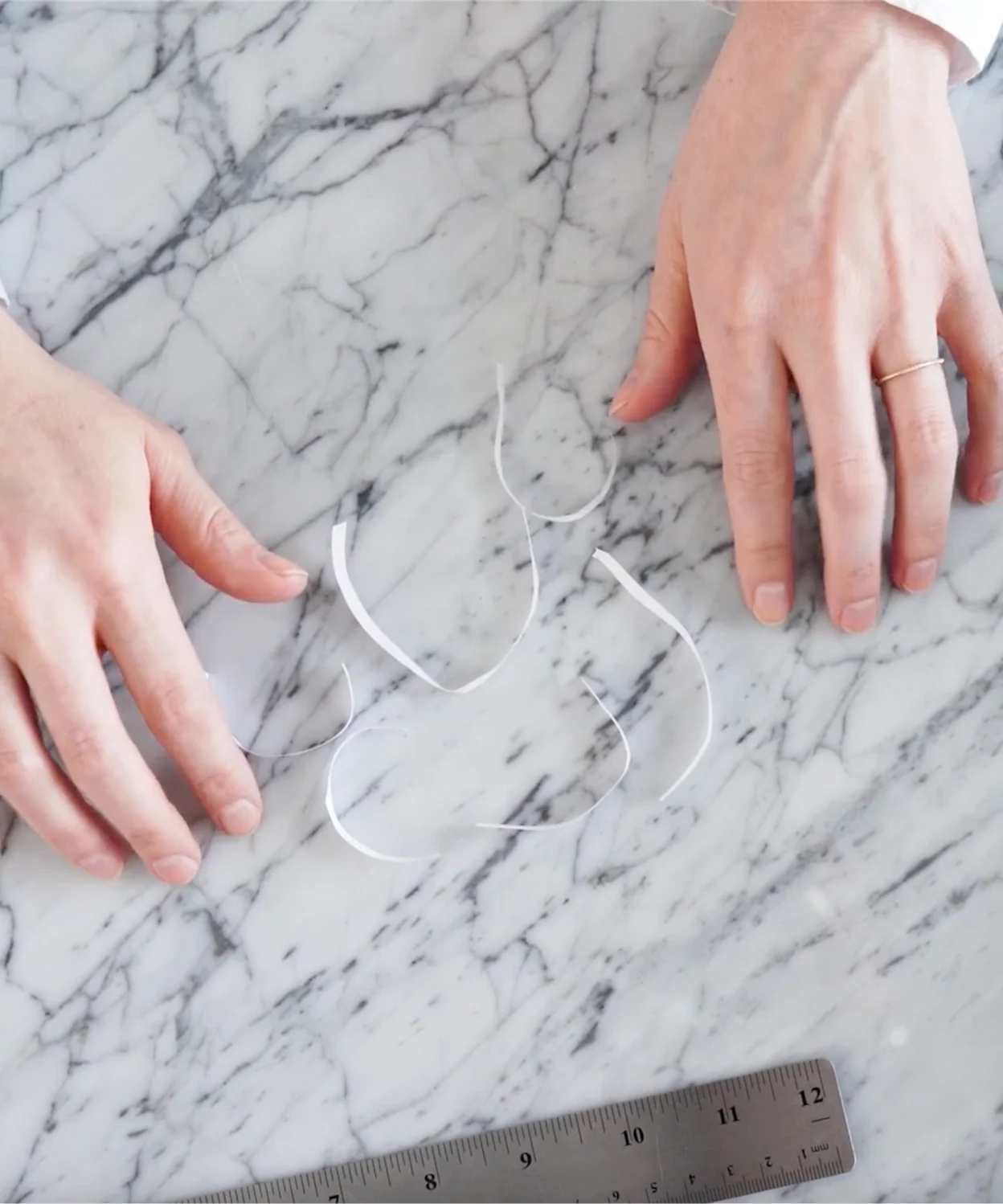 Paper strips and ruler on a marble surface, showing tools for measuring ring size at home.
